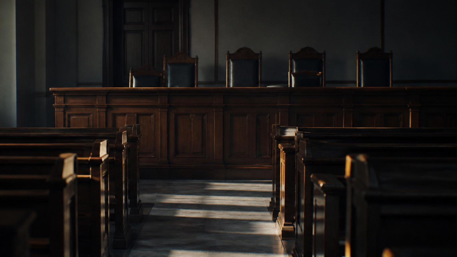 Empty wooden benches in a bare courtroom lit by daylight from tall side windows
