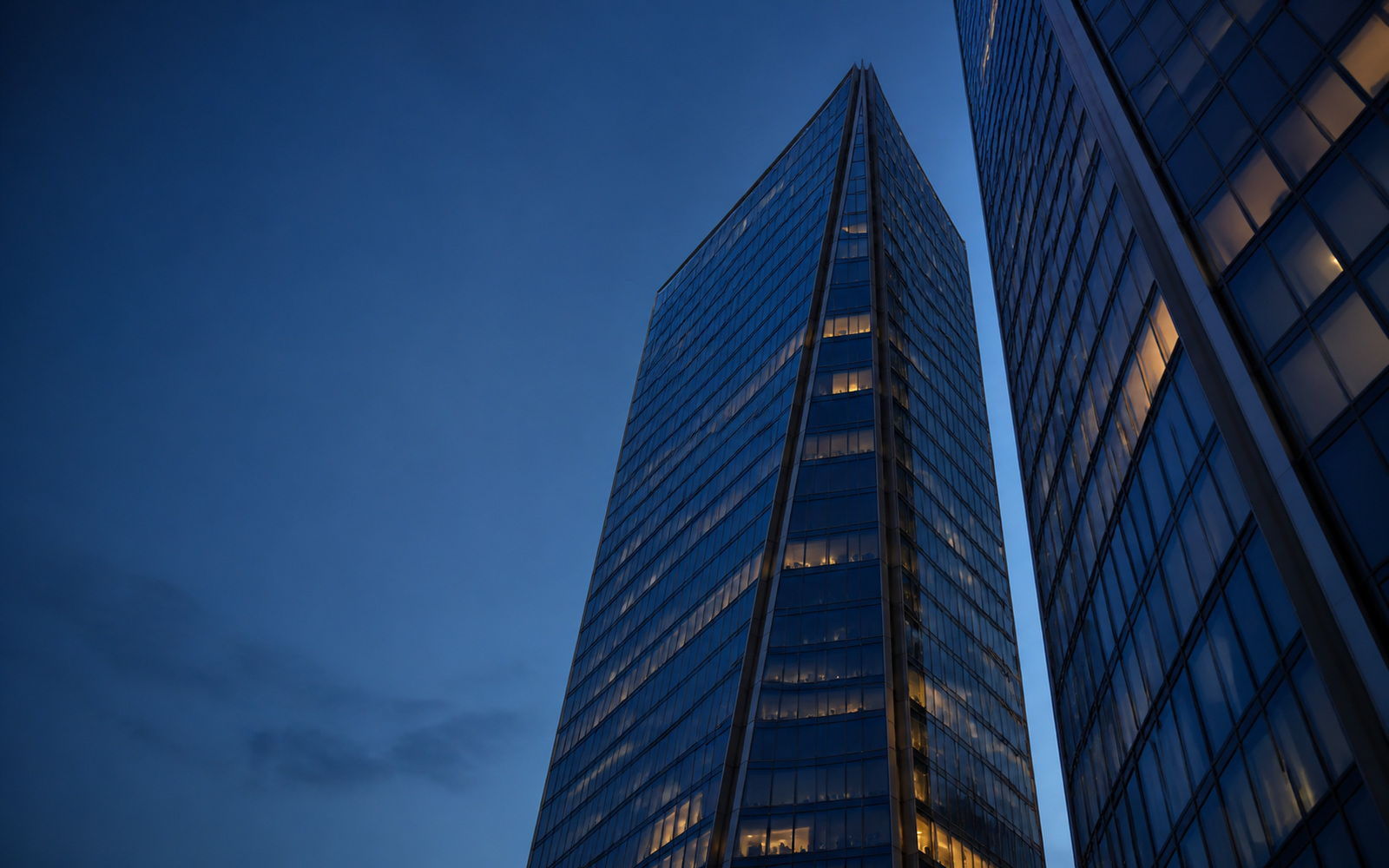 Two glass office towers seen from below, meeting at a narrow sky gap