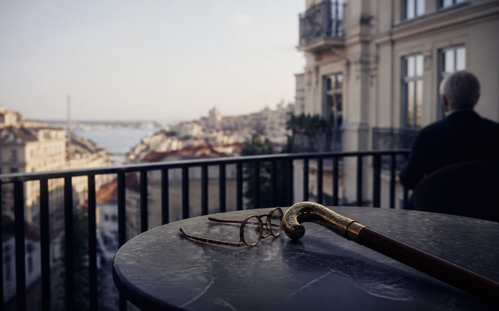 Walking stick and reading glasses on a sunlit balcony table above coastal apartment buildings
